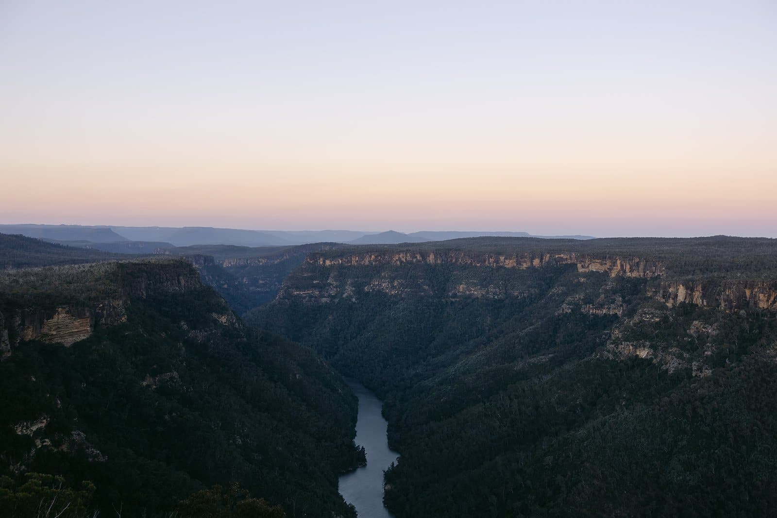 The Shoalhaven River winding far below the escarpment at Caoura Cliffs, the cliff line catching first light under a pink dawn sky